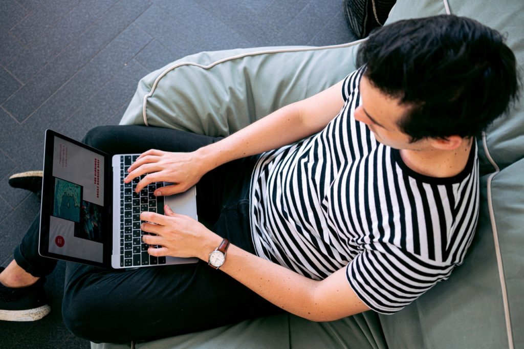 Man in striped shirt sitting on couch, working on laptop