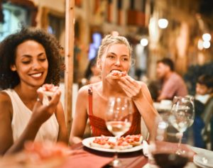 Two women eating dinner with white wine outside in town.